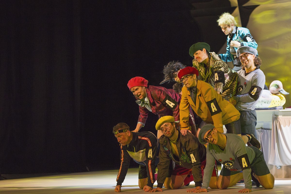Dziewięcioro aktorów stoi w akrobatycznej pozie, jeden na drugim.